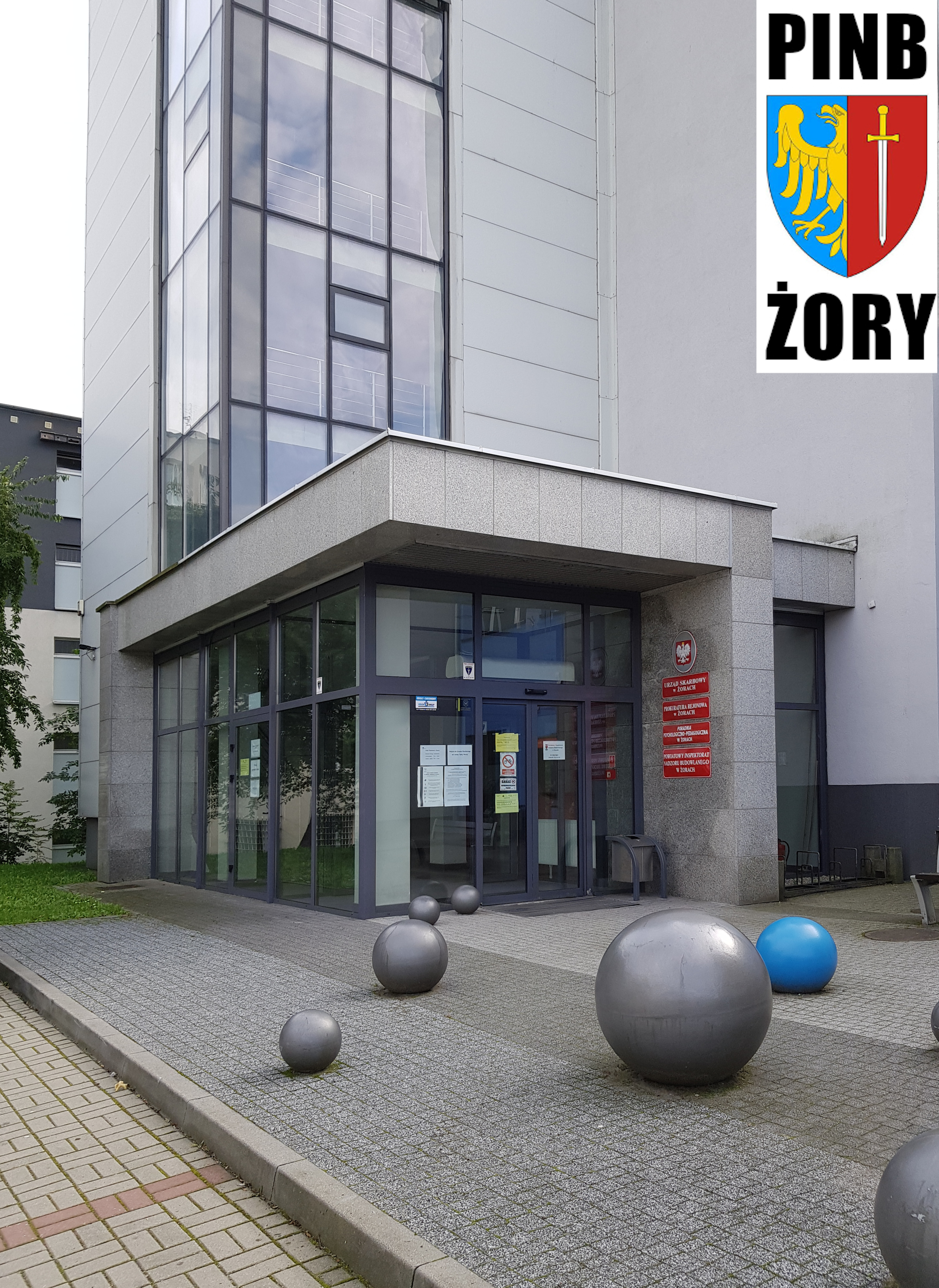 Zdjęcie wejścia do budynku przy ul. Wodzisławskiej 1 w Żorach. W prawym górnym rogu logo PINB.